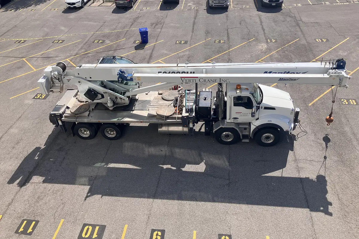 Telescopic boom truck crane with its boom raised, parked in a lot