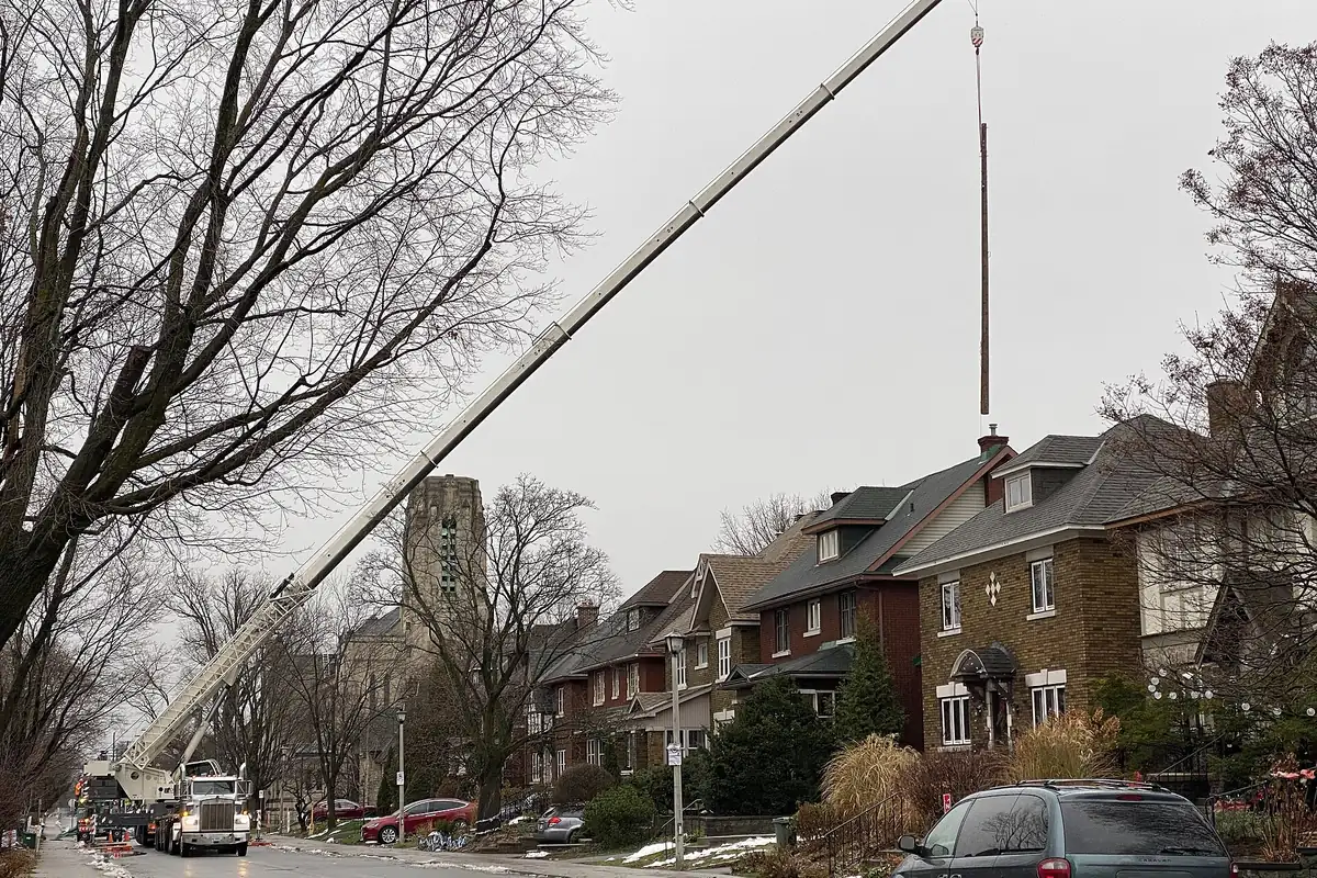 Truck-mounted crane lifting a utility pole over a row of houses