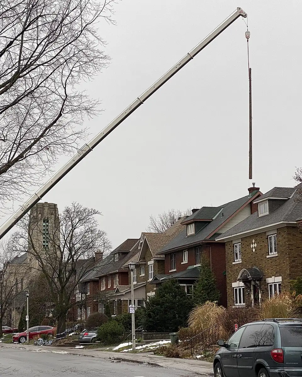 Truck-mounted hydraulic crane lifting a utility pole over a row of houses