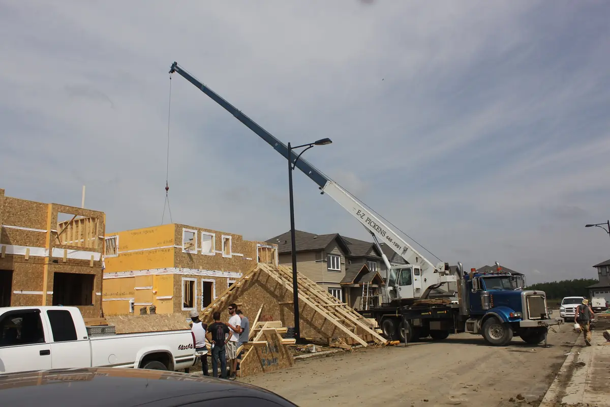 Boom truck lifting roof trusses onto a house under construction