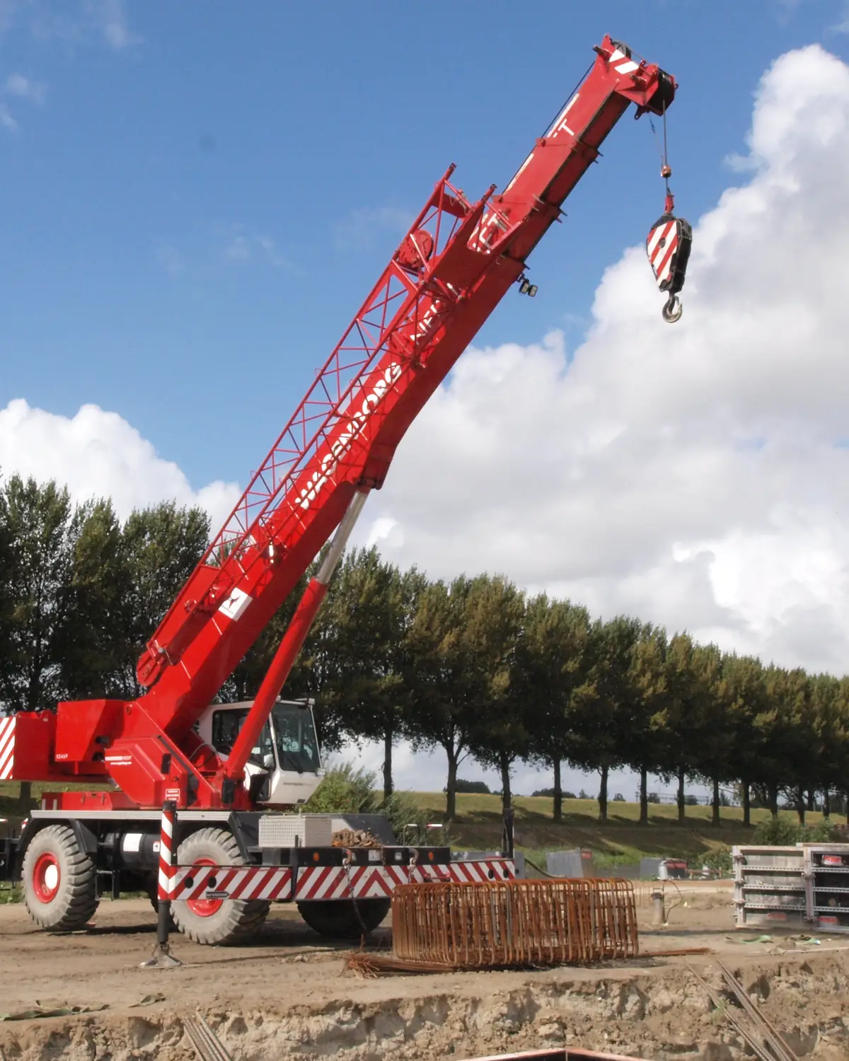 Red rough terrain crane on a dirt work site with its outriggers set and the hook raised